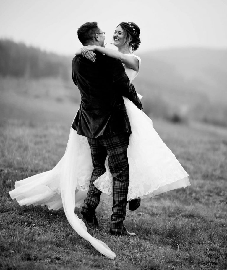 Groom picking up the bride and swinging her in black and white in a field.