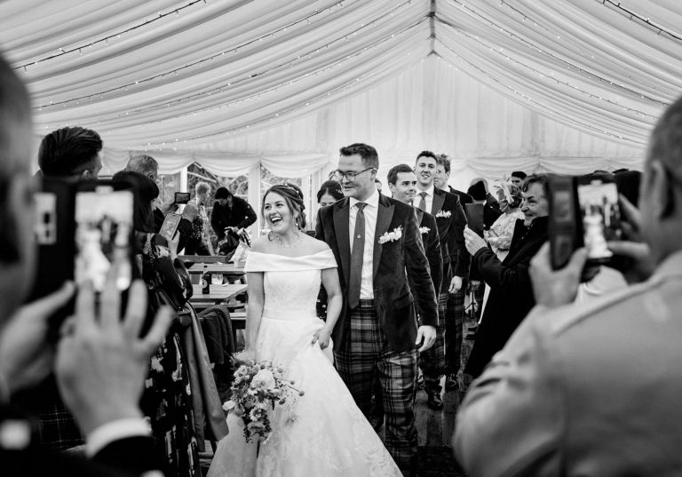 Couple walking into their reception in a marque in black and white