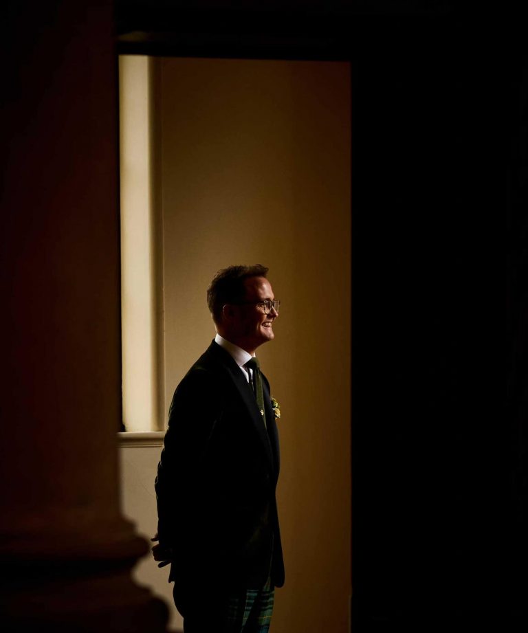 Groom lit with light from window in a room before wedding