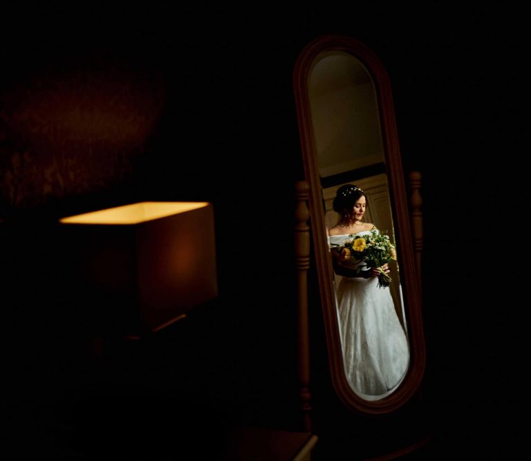 Bride reflection in the mirror holding flowers lit with window light