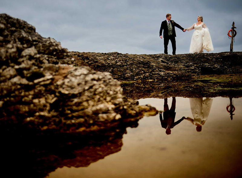 Bride and Groom on the beach holding hands their reflection in the water below for the best of 2025 weddings.